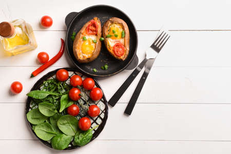 Baked sweet potato with egg and tomato on white table