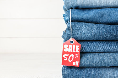 Stack of different jeans pants with shopping tag on white backgroundの写真素材