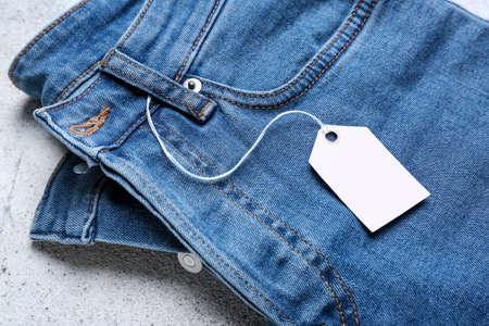 Jeans pants with shopping tag on light background