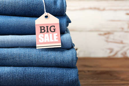 Stack of different jeans pants with shopping tag on wooden table