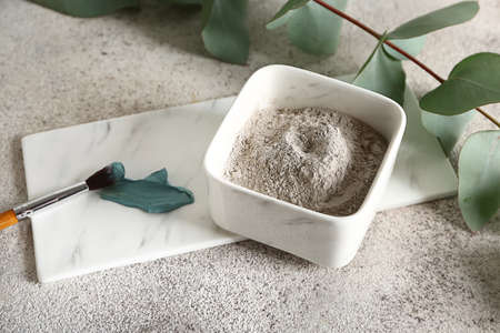 Cosmetic clay in bowl with brush on gray background