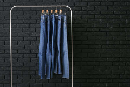 Clothes rack with stylish jeans pants near dark brick wallの写真素材