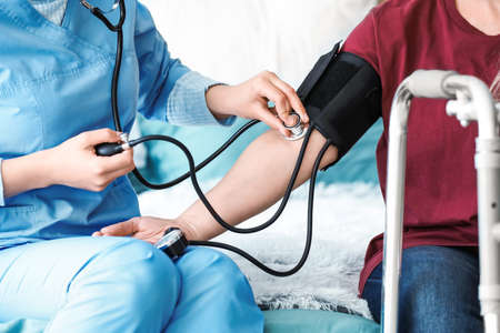 Medical assistant measuring blood pressure of mature patient at homeの写真素材