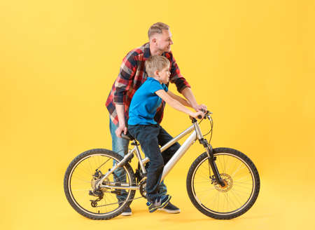 Father and his son with bicycle on color backgroundの写真素材