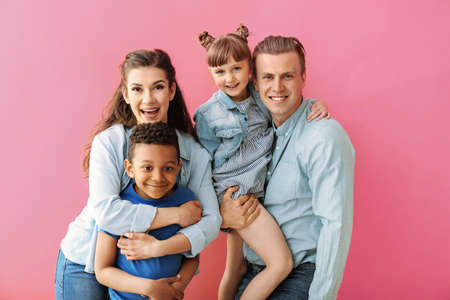 Happy couple with adopted children on color backgroundの写真素材
