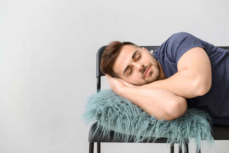 Handsome man sleeping on chairs against gray backgroundの写真素材