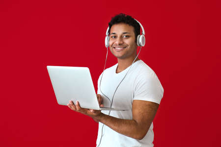 Handsome man with laptop and headphones on color backgroundの写真素材