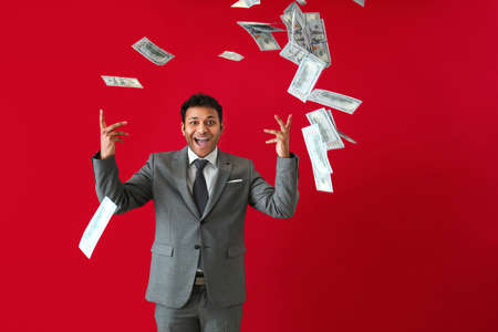 Happy businessman and falling dollar banknotes on color background