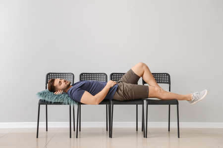 Handsome man sleeping on chairs near gray wall