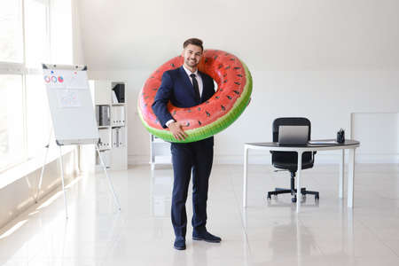 Handsome businessman with inflatable ring in office. Travel concept