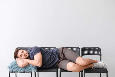 Handsome man sleeping on chairs against gray backgroundの写真素材
