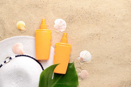 Bottles of sun protection cream, hat and seashells on sand