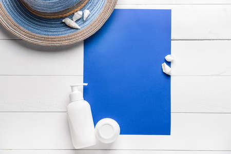Sun protection cream with sheet of paper, hat and seashells on wooden background