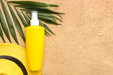 Bottle of sun protection cream and hat on sandの写真素材