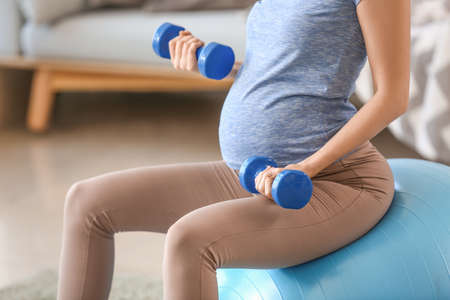 Beautiful pregnant woman with dumbbells and fitball training at homeの写真素材