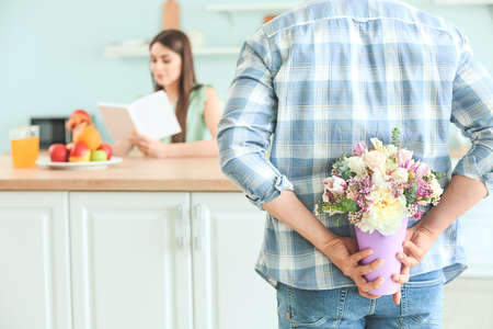 Young man hiding bouquet of flowers for his wife behind back at homeの写真素材