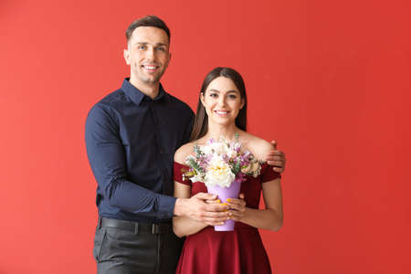 Young couple with bouquet of beautiful flowers on color backgroundの写真素材