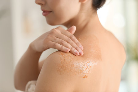 Beautiful young woman applying body scrub at home, closeupの写真素材