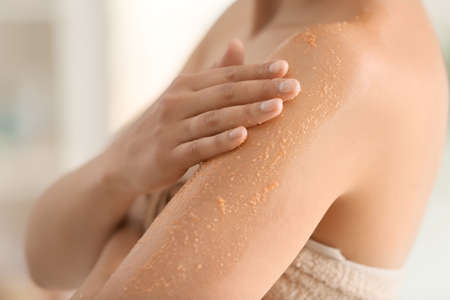 Beautiful young woman applying body scrub at home, closeupの写真素材