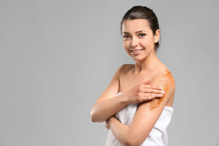 Beautiful young woman applying body scrub against gray backgroundの写真素材