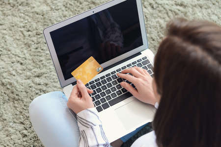 Young woman with credit card and laptop shopping online at homeの写真素材