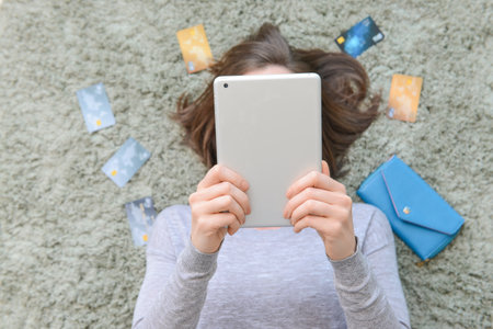 Young woman with credit cards and tablet computer lying on floor. Online shoppingの写真素材