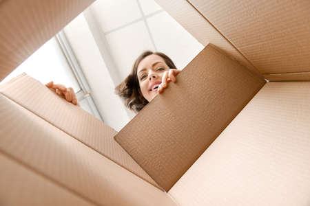 Young woman opening parcel at home, view from inside of boxの写真素材
