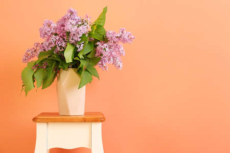 Beautiful lilac flowers in vase on table against color backgroundの写真素材