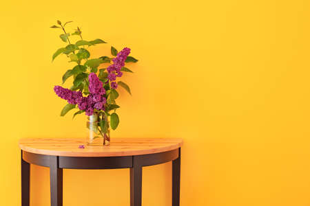 Beautiful lilac flowers in vase on table against color backgroundの写真素材