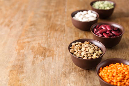 Bowls with different legumes on wooden background