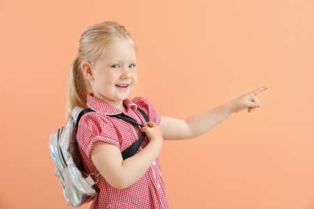 Portrait of adorable little girl pointing at something on color background
