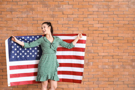 Happy young woman with national flag of USA on brick backgroundの写真素材