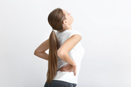 Young woman suffering from back pain on white background