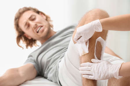 Man suffering from pain during wax epilation of legs in beauty salon