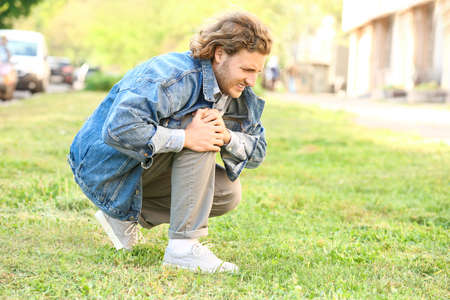 Young man suffering from pain in leg outdoorsの写真素材