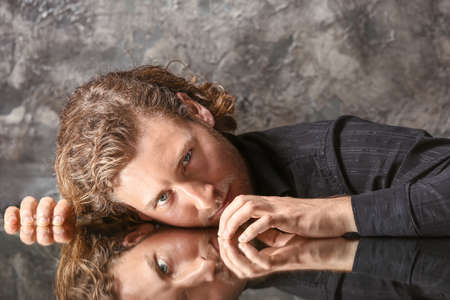 Stylish young man in fashionable clothes sitting at table with glass surfaceの写真素材