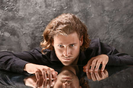 Stylish young man in fashionable clothes sitting at table with glass surfaceの写真素材