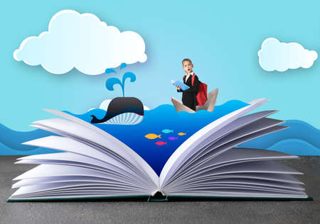 Open book with drawn sea and surprised little schoolgirl in paper boat on color backgroundの写真素材