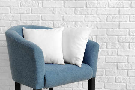 Soft pillows on armchair against white brick wall
