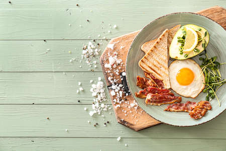 Plate with tasty fried egg, bacon, avocado and toasts on tableの写真素材
