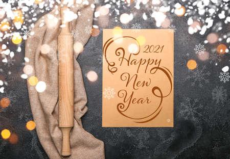 New Year composition with rolling pin and greeting card on dark background
