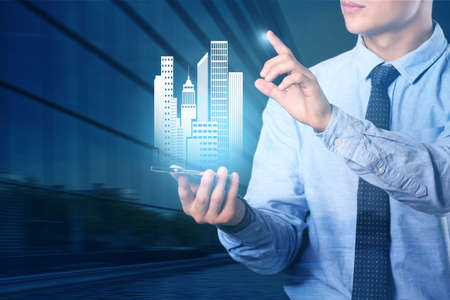 Young real estate agent with mobile phone using virtual screen on dark background