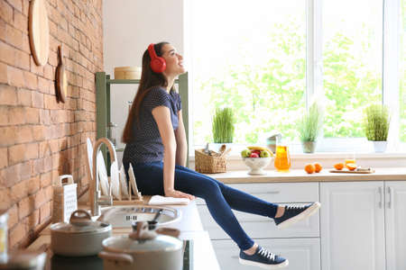 Beautiful woman listening to music in kitchen at homeの写真素材