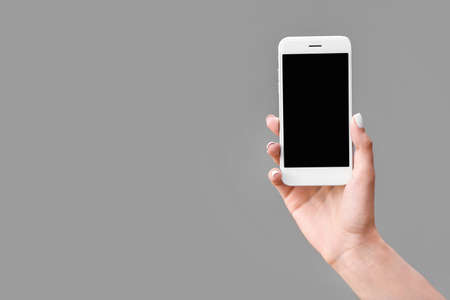 Female hand with mobile phone on gray backgroundの写真素材