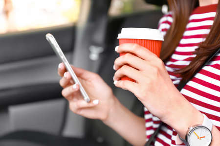 Young woman with mobile phone and coffee in car, closeup