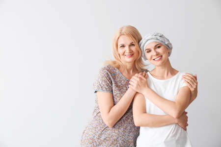 Woman after chemotherapy with her mother on light background