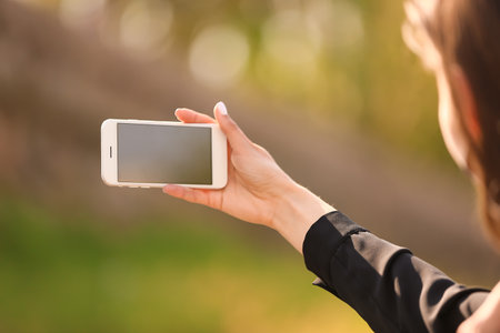 Young woman with mobile phone taking photo outdoorsの写真素材