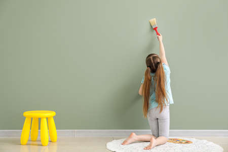 Cute little girl painting on wall in roomの写真素材