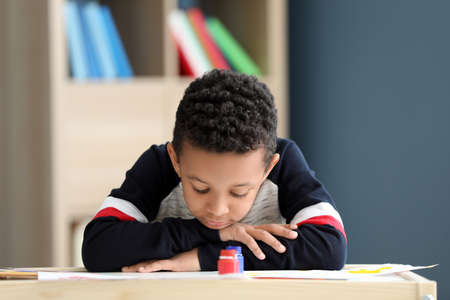 Cute African-American boy sitting at table in room