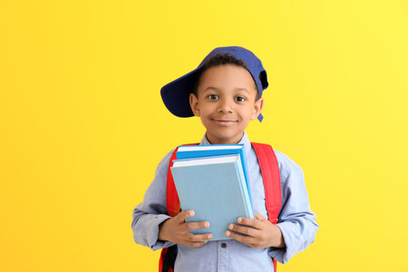 Cute African-American schoolboy on color background